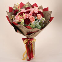 Blush Crimson Charm pink rose and red carnation bouquet with eucalyptus greenery, newspaper-style wrap, and red-gold ribbon by Rapid Petals by Yashken Fresh