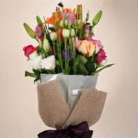 Tropical Rose Charm mixed flower bouquet with orange lilies, peach roses, pink roses, white blooms, purple fillers, greenery, clear wrap, and jute-style wrapping by Rapid Petals by Yashken Fresh